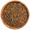 Rooibos met munt en cacaodoppen in een ronde houten kom op een witte achtergrond.